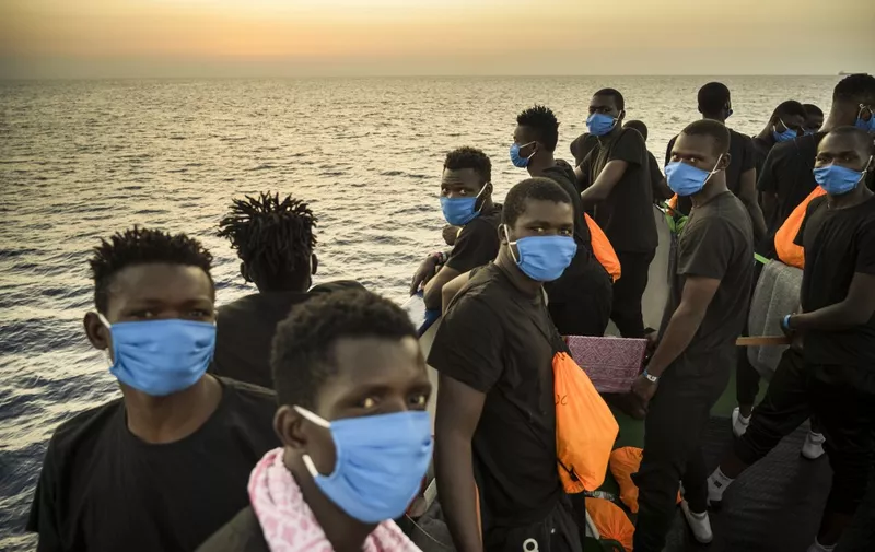 Migrants wearing face masks stand at sunset onboard the Sea-Watch 4 civil sea rescue ship react on sea off the coast of Sicily, Italy, on August 31, 2020. - More than 350 migrants are onboard the Sea-Watch 4, after it took more than 150 people from the German-flagged MV Louise Michel rescue vessel funded by British street artist Banksy. Sea-Watch 4, which has rescued 201 migrants before and is itself in search of a host port, decided to help the Louise Michel "in the face of the lack of reaction" from the authorities, a spokesman for the German NGO Sea-Watch, which charters the boat with Doctors Without Borders (MSF), told AFP. (Photo by Thomas Lohnes / AFP) / Germany OUT / The erroneous mention[s] appearing in the metadata of this photo by Thomas Lohnes has been modified in AFP systems in the following manner: [Migrants wearing face masks stand at sunset onboard the Sea-Watch 4 civil sea rescue ship react on sea off the coast of Sicily, Italy, on August 31, 2020.] instead of [Migrants onboard the Sea-Watch 4 civil sea rescue ship react on sea off the coast of Sicily, Italy, on September 01, 2020, as they learn that they have permission to run into the port of Palermo, Sicily, the next day.]. Please immediately remove the erroneous mention[s] from all your online services and delete it (them) from your servers. If you have been authorized by AFP to distribute it (them) to third parties, please ensure that the same actions are carried out by them. Failure to promptly comply with these instructions will entail liability on your part for any continued or post notification usage. Therefore we thank you very much for all your attention and prompt action. We are sorry for the inconvenience this notification may cause and remain at your disposal for any further information you may require.