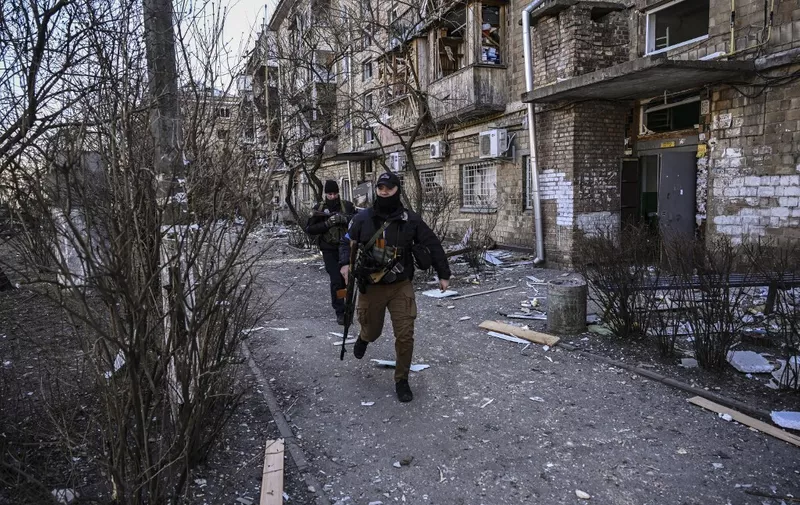 Ukranian servicemen run outside a destroyed apartment building in a residential area after shelling in Kyiv on March 18, 2022, as Russian troops try to encircle the Ukrainian capital as part of their slow-moving offensive. - Authorities in Kyiv said one person was killed early today when a downed Russian rocket struck a residential building in the capital's northern suburbs. They said a school and playground were also hit. (Photo by Aris Messinis / AFP)