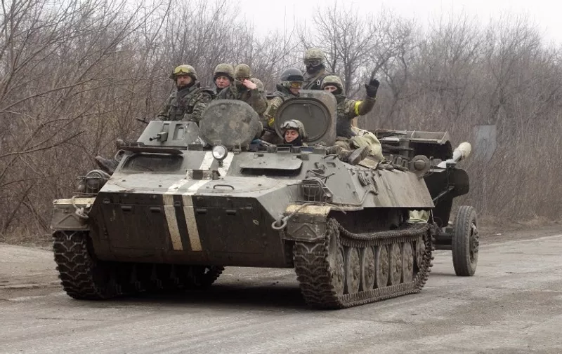 Soldiers gesture as an Ukrainian Armoured Personnel Carrier move a cannon from a position near eastern Ukrainian city of Artemivsk, in the Donetsk region on February 26, 2015. The Ukraine's military said it was starting the withdrawal of heavy weapons from the frontline with pro-Russian rebels, a key step in a stuttering peace plan. "Ukraine is beginning the withdrawal of 100mm cannons from the frontline. This is the first step in the pull-back of heavy weapons," the military said in a statement. AFP PHOTO/ ANATOLII STEPANOV