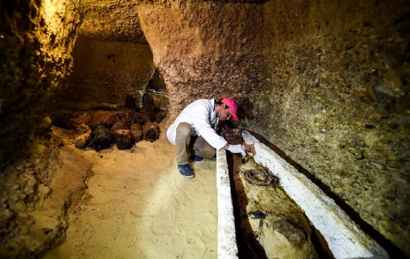 An archaeologist brushes a newly-discovered mummy laid inside a sarcophagus, part of a collection found in burial chambers dating to the Ptolemaic era (323-30 BC) at the necropolis of Tuna el-Gebel in Egypt's southern Minya province, about 340 kilometres south of the capital Cairo, on February 2, 2019. - Egypt's Antiquities Minister said on February 2 that a joint mission from the ministry and Minya University's Archaeological Studies Research Centre found upon a collection of Ptolemaic burial chambers engraved in rock and filled with a large number of mummies of different sizes and genders. The minister added that the newly discovered tombs may be a familial grave for a family from the elite middle class. (Photo by MOHAMED EL-SHAHED / AFP)