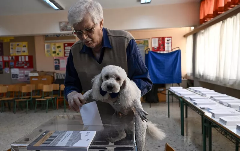 A voter carrying his dog casts his ballot at a polling station on the general elections day in Athens on May 21, 2023. Greece goes into the polls in fairly robust economic health, with unemployment and inflation falling and growth this year projected to reach twice that of the bloc -- a far cry from the throes of a crippling debt crisis a decade ago. (Photo by ARIS MESSINIS / AFP)