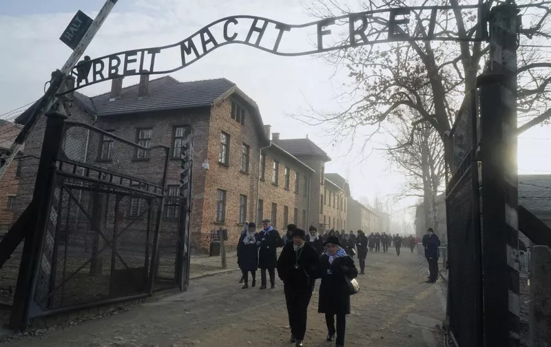 TOPSHOT - Holocaust survivors walk below the gate with its inscription "Work sets you free" after a wreath laying at the death wall at the memorial site of the former German Nazi death camp Auschwitz during ceremonies to commemorate the 75th anniversary of the camp's liberation in Oswiecim, Poland, on January 27, 2020. - More than 200 survivors are to come from across the globe to the camp the Nazis built in Oswiecim in then-occupied Poland, to share their testimony as a stark warning amid a recent surge of anti-semitic attacks on both sides of the Atlantic. (Photo by JANEK SKARZYNSKI / AFP)
