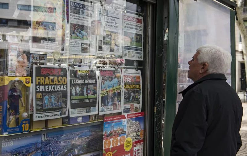 A man watches the front pages of sports newspapers on display in a kiosk in Barcelona on April 11, 2018 a day after the victory of AS Roma over FC Barcelona in the UEFA Champions League round of quarter-final second leg football match. Barcelona's shock Champions League exit at the hands of Roma does not discount what is likely to be a double-winning season but the loss should serve as a warning for what comes next. After the 3-0 defeat at Stadio Olimpico, which sent Roma through on away goals, Ernesto Valverde paid lip-service to shouldering responsibility but in the same breath pointed to a disappointment with his players. (Photo by Josep LAGO / AFP)