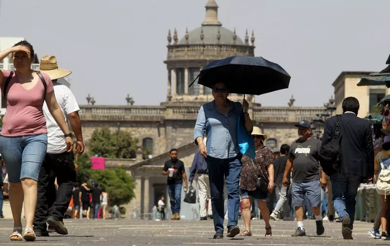 A group of people try to protect themselves from the intense sun during one of the hottest days of the third heat wave earlier this week that will see temperatures soar to levels normally not seen in Guadalajara, Jalisco state, Mexico on June 12. , 2023. (Photo by ULISES RUIZ / AFP)