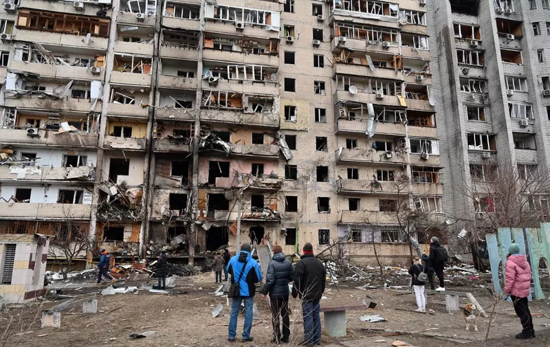 People look at a damaged residential building at Koshytsa Street, a suburb of the Ukrainian capital Kyiv, where a military shell allegedly hit, on February 25, 2022. - Invading Russian forces pressed deep into Ukraine as deadly battles reached the outskirts of Kyiv, with explosions heard in the capital early Friday that the besieged government described as "horrific rocket strikes". The blasts in Kyiv set off a second day of violence after Russian President Vladimir Putin defied Western warnings to unleash a full-scale ground invasion and air assault that quickly claimed dozens of lives and displaced at least 100,000 people. (Photo by GENYA SAVILOV / AFP)