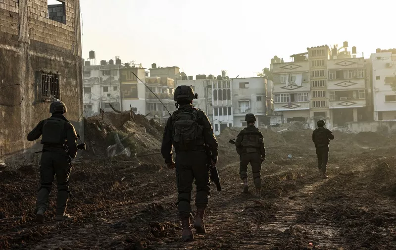 --PHOTO TAKEN DURING A CONTROLLED TOUR AND SUBSEQUENTLY EDITED UNDER THE SUPERVISION OF THE ISRAELI MILITARY-- This picture taken on December 19, 2023, shows Israeli soldiers walking past damaged buildings during a military operation in the north of the Gaza Strip amid continuing battles between Israel and the Palestinian militant group Hamas. (Photo by GIL COHEN-MAGEN / AFP)