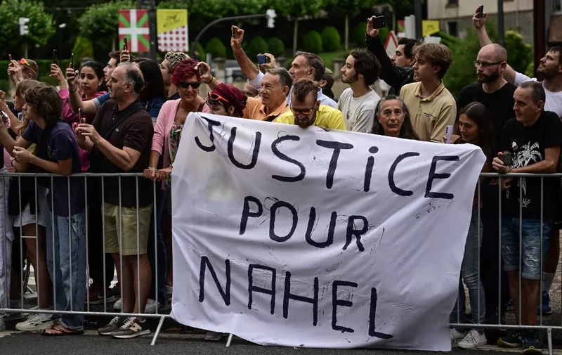 Spectator deploy a banner which reads "Justice for Nahel" along the race route at the start of the 1st stage of the 110th edition of the Tour de France cycling race, 182 km departing and finishing in Bilbao, in northern Spain, on July 1, 2023. Clashes continued across France despite the 45,000 police officers deployed, the highest number of any night since the start of the protests, backed by light armoured vehicles and elite police units. Police made more than 1,000 arrests and the country braced for more riots ahead of the funeral of the 17-year-old teenager who was killed by a police officer during a traffic stop. (Photo by Marco BERTORELLO / AFP)