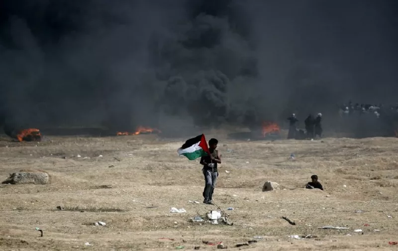 A man holds a Palestinian flag during clashes with Israeli forces near the border between the Gaza strip and Israel, east of Gaza City on May 14, 2018, following the the controversial move to Jerusalem of the United States embassy. 
Fifty-two Palestinians were killed by Israeli fire during violent clashes on the Gaza-Israel border coinciding with the opening of the US embassy in Jerusalem, the health ministry in the strip announced.
 / AFP PHOTO / THOMAS COEX