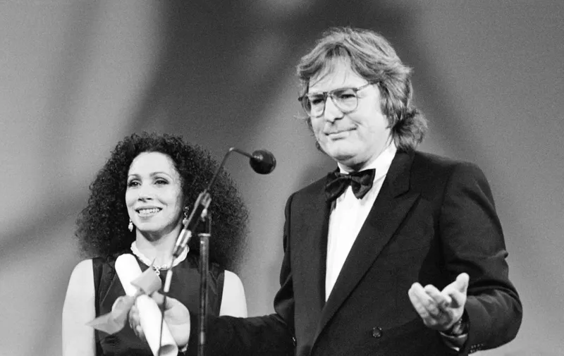 American filmmaker Alan Parker reacts as American Opera singer Julia Migenes-Johnson looks on, after Parker was awarded with the Grand Prix Special du Jury for his film "Birdy" at the 38th Cannes film Festival, on May 20, 1985. AFP PHOTO/RALPH GATTI (Photo by RALPH GATTI / AFP)