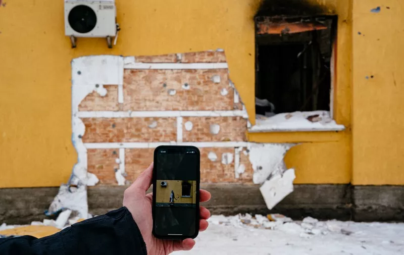 This photograph taken on December 3, 2022 shows a mobile phone with Banksy's work on the screen in front of a cut off of the wall of a damaged building from where a group of people tried to steal this work of the famous British artist in the town of Gostomel, near Kyiv, amid the Russian invasion of Ukraine. - Ukraine has detained eight people over the theft from a wall in the Kyiv suburbs of a mural painted by elusive British street artist Banksy, the authorities said. "A group of people tried to steal a Banksy mural. They cut out the work from the wall of a house destroyed by the Russians," Kyiv governor Oleksiy Kuleba said in a post on Telegram. (Photo by Dimitar DILKOFF / AFP)