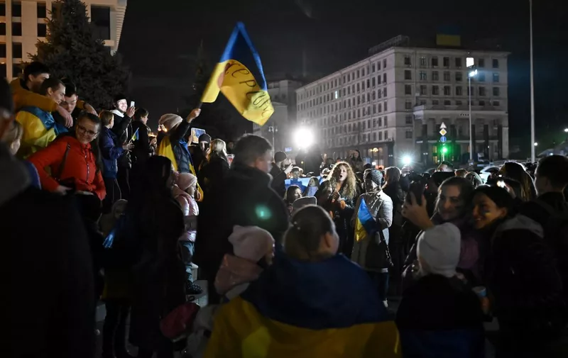 People hold a Ukranian flag as they gather in Maidan square to celebrate the liberation of Kherson, in Kyiv on November 11, 2022, amid the Russian invasion of Ukraine. - Ukraine's President Volodymyr Zelensky said on November 11 that Kherson was "ours" after Russia announced the completion of its withdrawal from the regional capital, the only one Moscow captured in nearly nine months of fighting. (Photo by Genya SAVILOV / AFP)