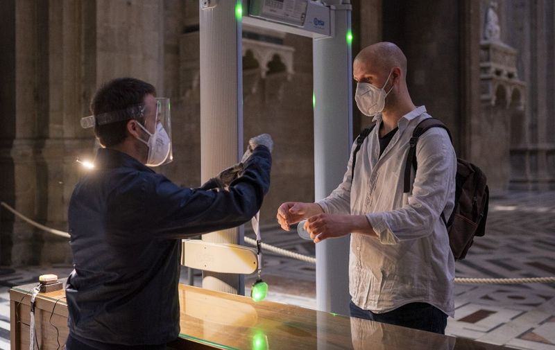 A photo taken and handout on May 21, 2020 by the press office of Florence's Duomo Museum (Opera Duomo Firenze) shows an attendant (L) handing to a visitor a new device that allows to maintain a safe distance between visitors, during testing on the eve of the museum's and Florence's Duomo reopening as the country eases its lockdown aimed at curbing the spread of the COVID-19 infection, caused by the novel coronavirus. - The small device, distributed free of charge at the beginning of a visit and returned at the end to be sanitized, signals with a sound, vibration and light when the minimum allowed distance between visitors is being exceeded. (Photo by Handout / FLORENCE MUSEUM PRESS OFFICE / AFP) / RESTRICTED TO EDITORIAL USE - MANDATORY CREDIT "AFP PHOTO / FLORENCE MUSEUM PRESS OFFICE / HANDOUT" - NO MARKETING - NO ADVERTISING CAMPAIGNS - DISTRIBUTED AS A SERVICE TO CLIENTS
