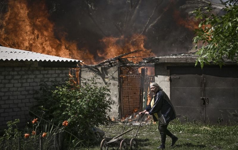 An elderly woman walks away from a burning house garage after shelling in the city of Lysytsansk at the eastern Ukrainian region of Donbas on May 30, 2022, on the 96th day of the Russian invasion of Ukraine. - Since failing to capture Kyiv in the war's early stages, Russia's army has narrowed its focus, hammering Donbas cities with artillery and missile barrages as it seeks to consolidate its control. (Photo by ARIS MESSINIS / AFP)