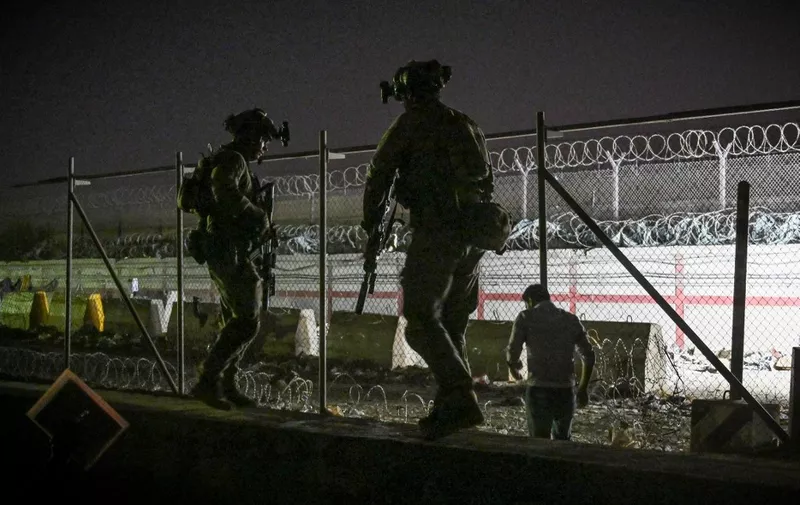 In this picture taken in the late hours on August 22, 2021 British and Canadian soldiers stand guard near a canal as Afghans wait outside the foreign military-controlled part of the airport in Kabul on August 23, 2021, hoping to flee the country following the Taliban's military takeover of Afghanistan. (Photo by WAKIL KOHSAR / AFP)