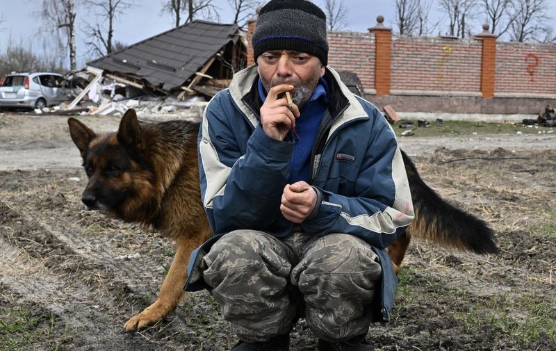 A man with a dog smokes as he sits in front of a destroyed house in Bohdanivka village, northeast of Kyiv, on April 12, 2022. - While Russia appears to have abandoned for now its aim of pushing deep into the heart of Ukraine, its new declared goal of taking control of much of the east of the country still risks a protracted and bloody conflict. (Photo by Genya SAVILOV / AFP)
