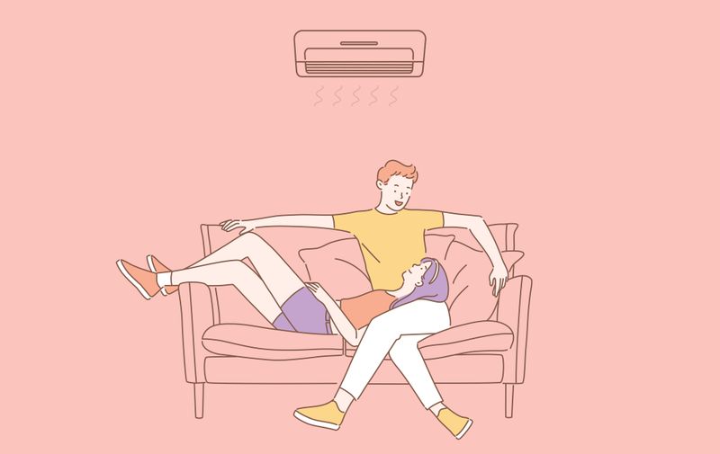 Air conditioning, climatic control, comfort concept. Couple in love relaxing under the air conditioner at home. Young happy guy and girl enjoy cool on hot summer day at home or in office.