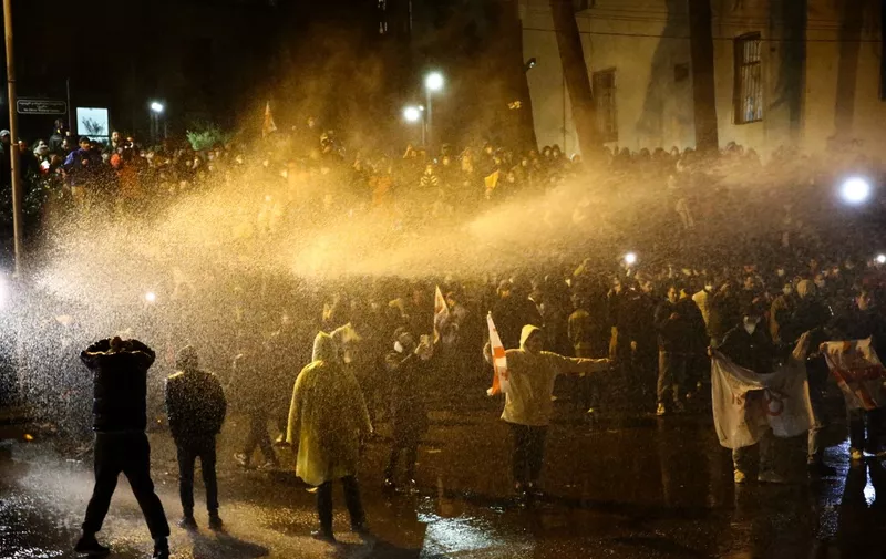 Protesters are sprayed by a water cannon during clashes with riot police near the Georgian parliament in Tbilisi late on March 8, 2023. - Georgian police fired water cannon and tear gas at thousands of protesters Wednesday, ordering them to disperse as they rallied against a planned "foreign agent" law reminiscent of Russian legislation used to silence critics. (Photo by Zurab Tsertsvadze / AFP)