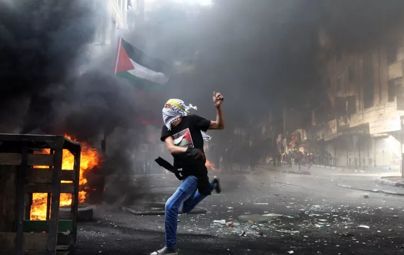 A masked Palestinian hurls rocks towards Israeli soldiers during clashes following the funeral of Mohammed Fares al-Jaabari on October 10, 2015, in the center of the West Bank town of Hebron. Israeli security forces have arrested approximately 400 Palestinians since the October 1 outbreak of violence in the occupied West Bank and annexed east Jerusalem, the Palestinian Prisoner Club said. AFP PHOTO / HAZEM BADER