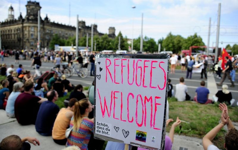 An anti-racism protesters sit behind a banner with the lettering "Refugees Welcome" during a rally on August 29, 2015 in Dresden, stronghold of the anti-Islam PEGIDA movement, whose demonstrations drew up to 25,000 at the start of the year. Activists demonstrate in solidarity with migrants, in a show of defiance against far-right extremists who have mounted noisy protests against a record influx of migrants to Germany. AFP PHOTO / ROBERT MICHAEL