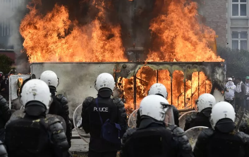 Police forces stand next to a car fire during a demonstration of farmers on September 7, 2015 in Brussels, as European agriculture ministers hold an extraordinary meeting at the European Council. 
Belgian police on September 7 fired water cannons at European farmers who lobbed hay and fireworks as they demanded EU intervention against plunging food prices partly blamed on a Russian embargo. The European Commission said it would release 500 million euros ($557 million) in emergency funds to help ease the pressure on farmers. AFP PHOTO/JOHN THYS