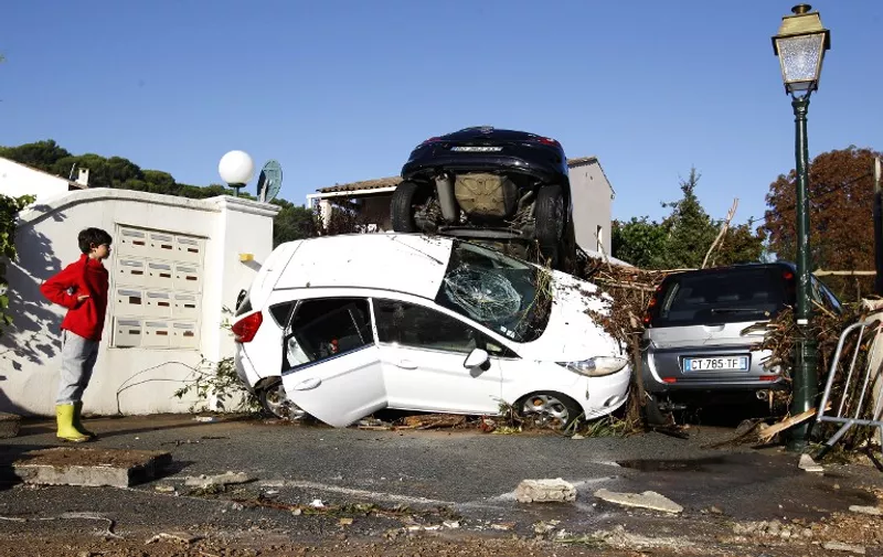 A boy stands next to rubble and damaged cars after violent storms and floods in Biot, southeastern France, on October 4, 2015. Violent floods along the French riviera killed 13 people by early Sunday, emergency responders and local officials said, including three who drowned in a retirement home inundated when a river broke its banks.AFP PHOTO / JEAN CHRISTOPHE MAGNENET