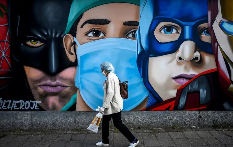A woman wearing a protective face mask walks past a mural depicting a medical worker among well-known fictional super heroes in Novi Sad on May 23, 2020. - Balkan countries coped with the COVID-19 pandemic with relative success, with fewer than 20,000 people infected and around 650 deaths in a region of some 22 million people. (Photo by Andrej ISAKOVIC / AFP)