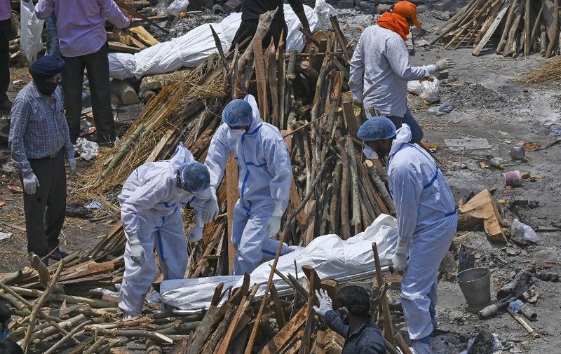 Family members and ambulance worker wearing PPE kit (Personal Protection Equipment) carry the bodies of the patients who died of the Covid-19 coronavirus at a cremation ground in New Delhi on April 27, 2021. (Photo by Prakash SINGH / AFP)