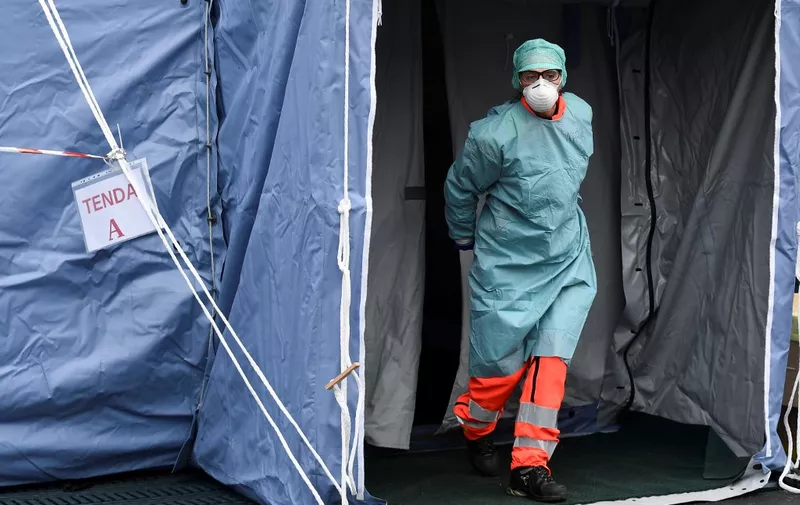 A hospital employees wearing a protection mask and gear exits a tent at a temporary emergency structure set up outside the accident and emergency department, where any new arrivals presenting suspect new coronavirus symptoms are being tested, at the Brescia hospital, Lombardy, on March 13, 2020. (Photo by MIGUEL MEDINA / AFP)