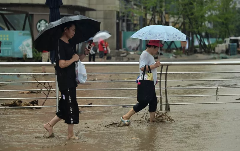 People walk along a water laden street, after heavy rains in Mentougou district in Beijing on July 31, 2023. Heavy rains battered northern China on July 31, killing at least two people in Beijing while washing away cars and inundating subway stations, with the capital issuing its highest alerts for flooding and landslides. (Photo by Pedro PARDO / AFP)