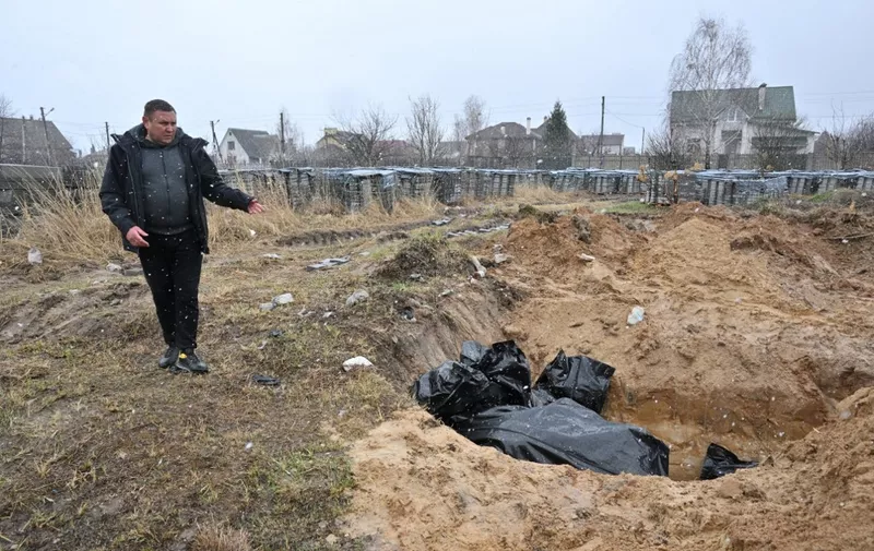 A man gestures at a mass grave in the town of Bucha, northwest of the Ukrainian capital Kyiv on April 3, 2022. - Ukraine and Western nations accused Russian troops of war crimes after the discovery of mass graves and "executed" civilians near Kyiv, prompting vows of action at the International Criminal Court. City mayor Anatoly Fedoruk told AFP that 280 other bodies had been buried in mass graves. One rescue official said 57 people were found in one hastily dug trench behind a church. (Photo by Sergei SUPINSKY / AFP)