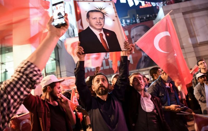 A supporter of the "yes" brandishes a picture of Turkish president Recep Tayyip Erdogan among other supporters waving Turkish national flags during a rally near the headquarters of the conservative Justice and Development Party (AKP) on April 16, 2017 in Istanbul after the initial results of a nationwide referendum that will determine Turkey's future destiny.
The "Yes" campaign to give Turkish President expanded powers was just ahead in a tightly-contested referendum but the 'No' was closing the gap, according to initial results. / AFP PHOTO / OZAN KOSE