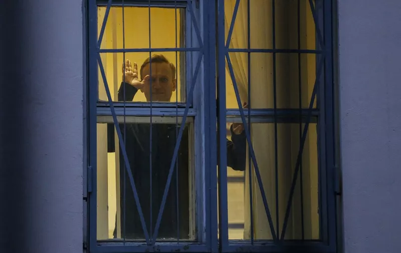 Russian opposition leader Alexei Navalny waves from behind the window of a police station in Moscow on September 29, 2017. - Alexei Navalny, who aims to unseat Vladimir Putin in presidential elections next year, was detained ahead of a rally on September 29, 2017, raising the possibility of a month in jail. (Photo by Maxim ZMEYEV / AFP)