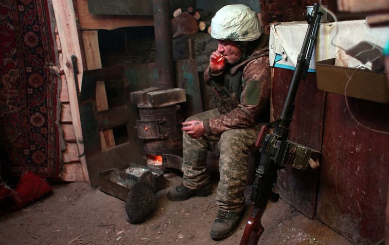 An Ukrainian Military Forces serviceman smokes in a dugout, as he and a cat sit near a wood burner on the frontline with the Russia-backed separatists near Zolote village, in the eastern Lugansk region, on January 21, 2022. - Ukraine's Foreign Minister Dmytro Kuleba on January 22, 2022, slammed Germany for its refusal to supply weapons to Kyiv, urging Berlin to stop "undermining unity" and "encouraging Vladimir Putin" amid fears of a Russian invasion. (Photo by Anatolii STEPANOV / AFP)