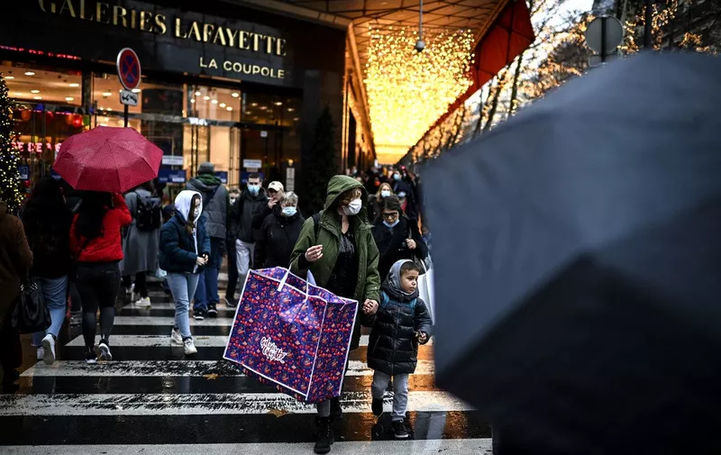 A woman carries a shopping bag past an entrance of the Galeries Lafayette department store in Paris on December 23, 2020, the day before Chritsmas' eve. (Photo by Christophe ARCHAMBAULT / AFP)