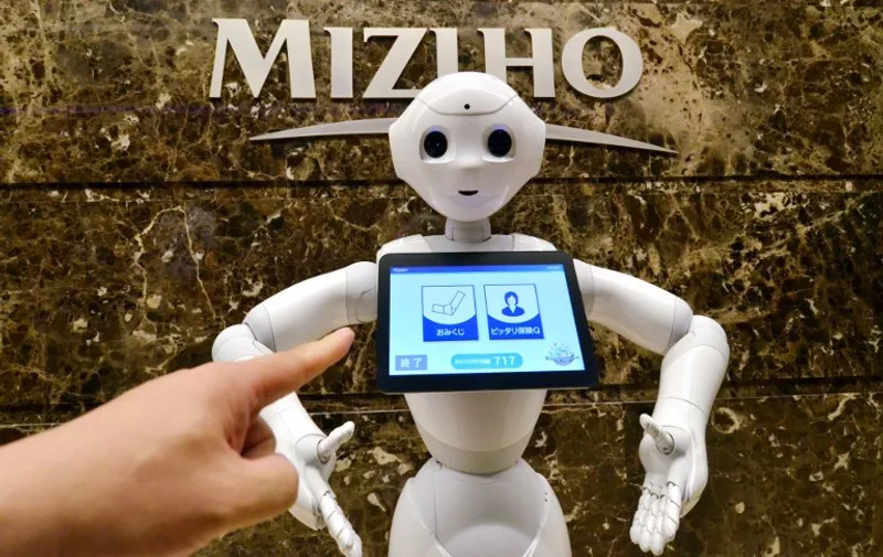 An employee (L) of Japan's Mizuho Bank provides a demonstration on how to operate Softbank's humanoid robot Pepper at the bank's headquarters in Tokyo on July 17, 2015. The Japanese bank hired Pepper robots as the world's first robotic bank concierges to greet customers and explain financial products at the bank's headquarters and branches in the Tokyo metropolitan area. AFP PHOTO / Yoshikazu TSUNO