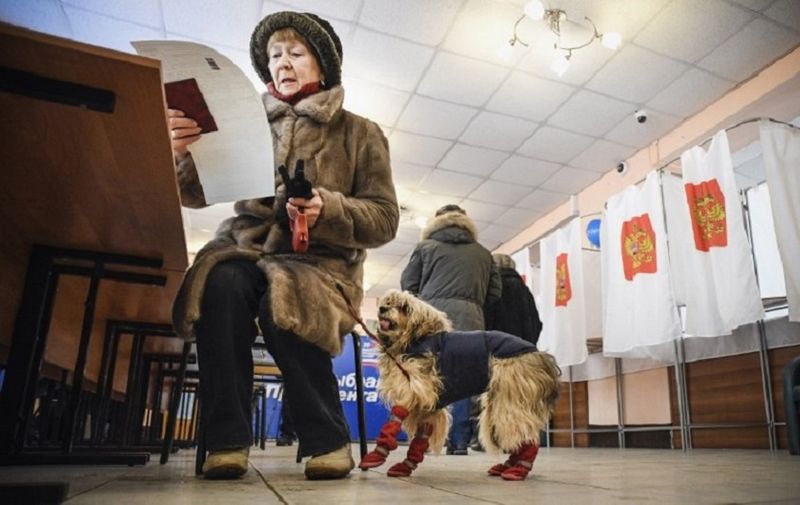 A woman with a dog reads her ballot at a polling station during Russia's presidential election in Moscow on March 18, 2018. / AFP PHOTO / Alexander NEMENOV