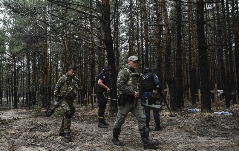 Ukrainian servicemen search for land mines at a burial site in a forest on the outskirts of Izyum, eastern Ukraine on September 16, 2022. - Ukraine said on September 16, 2022 it had counted 450 graves at just one burial site near Izyum after recapturing the eastern city from the Russians. (Photo by Juan BARRETO / AFP)
