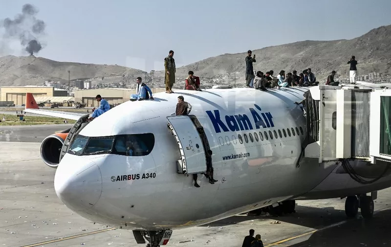 Afghan people climb atop a plane as they wait at the airport in Kabul on August 16, 2021, after a stunningly swift end to Afghanistan's 20-year war, as thousands of people mobbed the city's airport trying to flee the group's feared hardline brand of Islamist rule. (Photo by Wakil Kohsar / AFP)