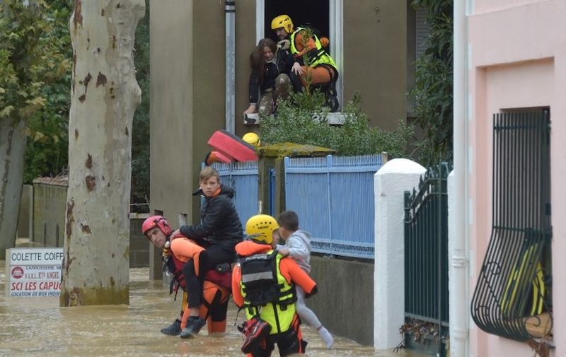 Firefighters help youngsters to evacuate in a flooded street during a rescue operation following heavy rains that saw rivers bursting banks on October 15, 2018 in Trebes, near Carcassone, southern France. - Six people died following storm and flash floods during the night of October 15 in the Aude department in southern France, authorities said. (Photo by Pascal PAVANI / AFP)