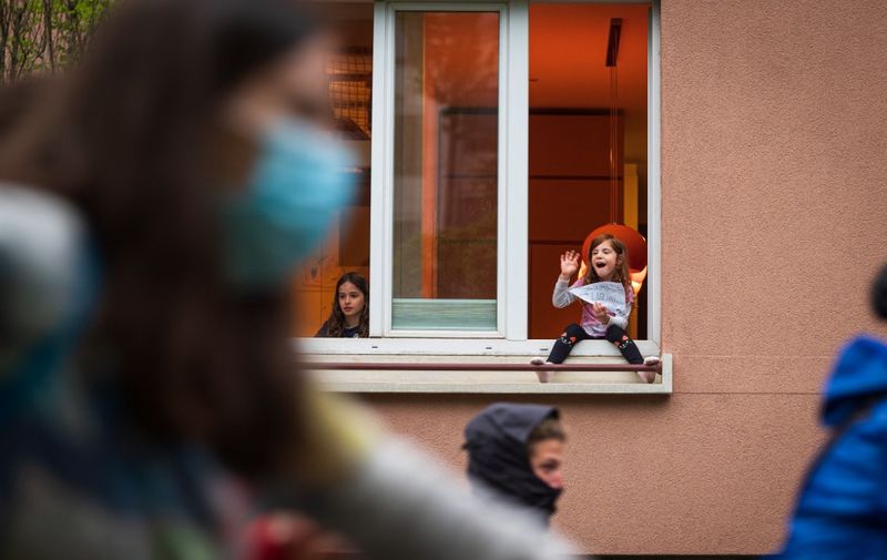 A girl sits on a window shelf and waves to protesters, some wearing face masks, as they ride their bicycles and block the centre of the capital Ljubljana, on May 15, 2020, during a demonstration to protest against the centre-right government, accusing it of corruption and of using the COVID-19 (the novel coronavirus) crisis to restrict freedom. (Photo by Jure Makovec / AFP)