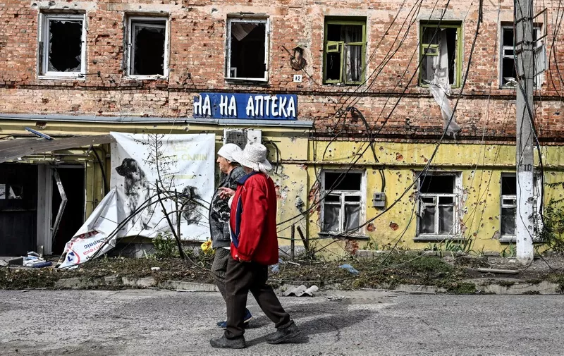 Two women walk in front of a destroyed building in the village of Kupiansk, eastern Ukraine, in September 17, 2022, amid the Russian invasion of Ukraine. (Photo by Juan BARRETO / AFP)