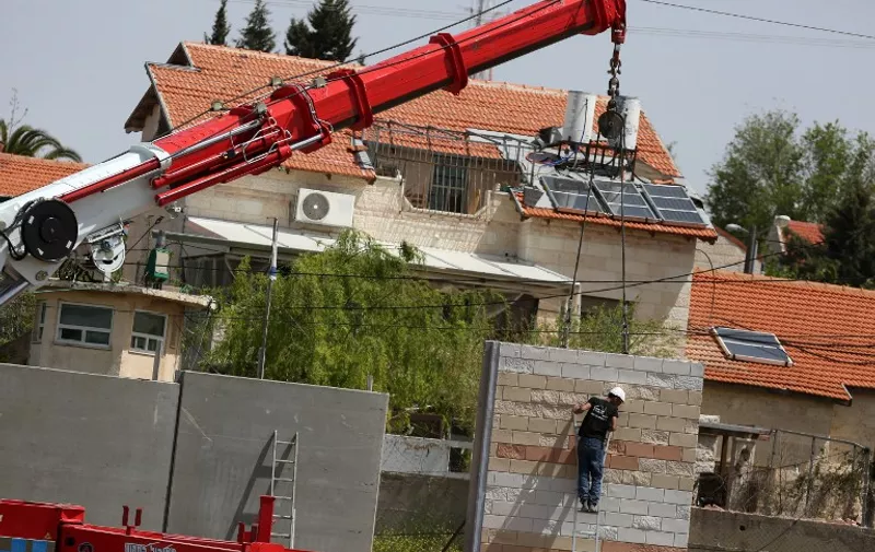An Israeli crane lifts a section of concrete as they build a defensive wall arround the Israeli settlement of Beit El, in the occupied West Bank north of Ramallah on April 7, 2015, next to a road used by Palestinians from the adjacent Jalazon refugee camp. AFP PHOTO/ABBAS MOMANI