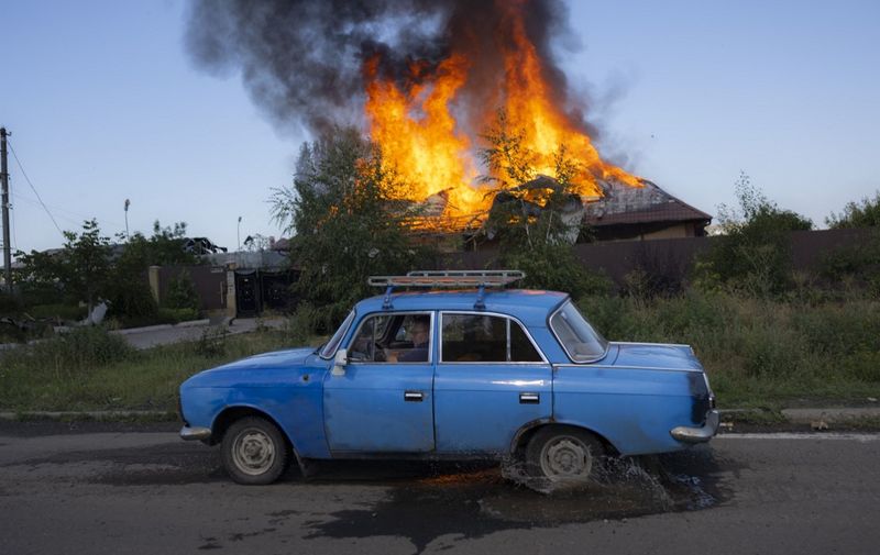 A Ukrainien man drives past a burning house hit by a shell in the outskirts of Bakhmut, Eastern Ukraine, on July 27, 2022, amid the Russian invasion of Ukraine. (Photo by BULENT KILIC / AFP)