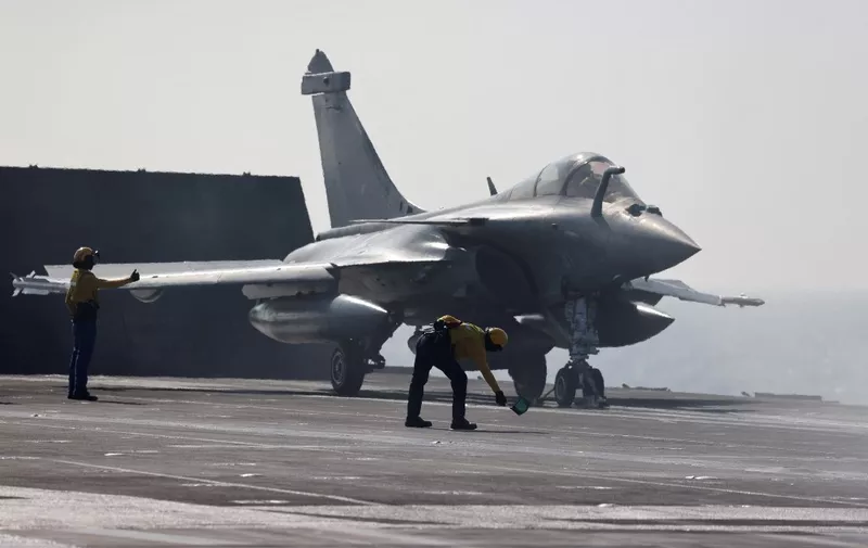 French navy aircraft handling officers, known as a "Chien Jaune" (French for "yellow dog") signal to a Rafale aircraft fighter for takeoff from the flight deck of the French aircraft carrier Charles de Gaulle, sailing between the Suez canal and the Red Sea on December 19, 2022. - French President Emmanuel Macron will join the French aircraft carrier Charles de Gaulle on December 19, 2022 for the traditional Christmas party with the troops, before attending a regional conference in Jordan on December 20, the Elysee presidential palace announced. (Photo by Ludovic MARIN / POOL / AFP)