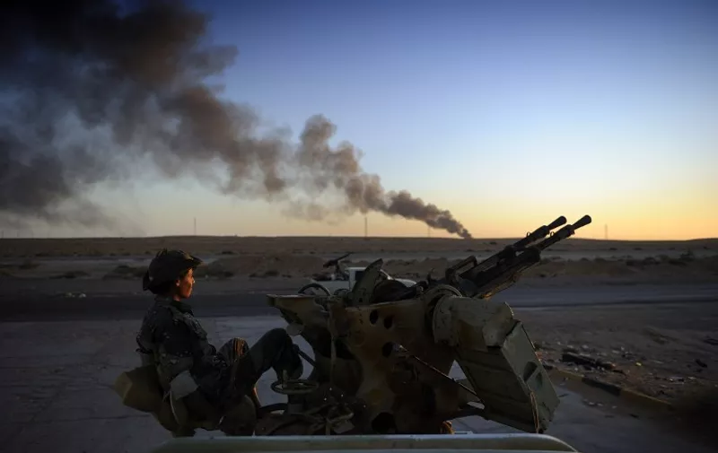A rebel fighter looks on as he sits on an anti-aircraft machine gun on August 29, 2011 near Ras Lanuf while smoke pours from a rafinery. The insurgents prepare to launch an assault on Kadhafi's hometown of Sirte after routing his forces in the capital Tripoli a week ago. The chiefs of staff of countries militarily involved in the Libyan conflict agreed that the war in the North African country was not over yet.  AFP PHOTO / ERIC FEFERBERG / AFP / ERIC FEFERBERG