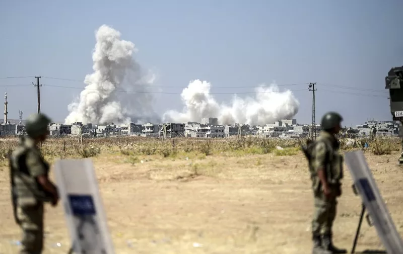 A picture taken from the Turkish side of the border in Suruc, Sanliurfa province, shows Turkish soldiers standing as smoke rises from the Syrian town of Kobane, also known as Ain al-Arab, on June 27, 2015, a day after a deadly suicide bombing occurred. The Islamic State group killed 164 civilians in its offensive on the Kurdish town of Kobane, in what a monitor Friday called one of the jihadists' "worst massacres" in Syria. AFP PHOTO/BULENT KILIC