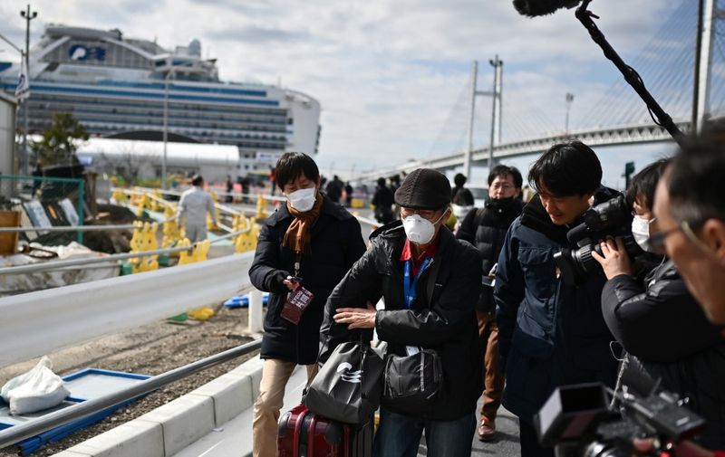 A passenger (C) leaves on foot after dismembarking the Diamond Princess cruise ship (back, L) in quarantine due to fears of the new COVID-19 coronavirus, at the Daikoku Pier Cruise Terminal in Yokohama on February 19, 2020. - Relieved passengers began leaving a coronavirus-wracked cruise ship in Japan on February 19 after testing negative for the disease that has now claimed more than 2,000 lives in China. (Photo by CHARLY TRIBALLEAU / AFP)
