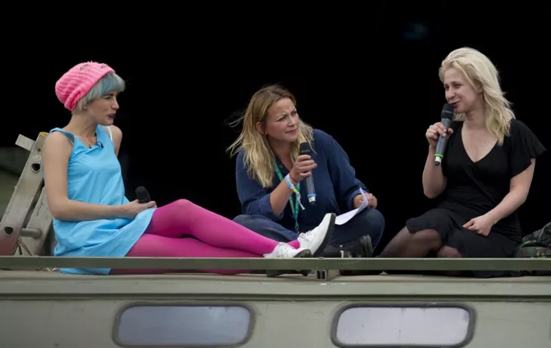 Members of Russian punk rock protest group Pussy Riot, Nadezhda Tolokonnikova (L) and Maria Alyokhina (R) speak with Welsh singer Charlotte Church from on top of a Russian military vehicle at The Park stage on the first official day of the Glastonbury Festival of Music and Performing Arts on Worthy Farm near the village of Pilton in Somerset, South West England, on June 26, 2015.  
 AFP PHOTO / OLI SCARFF / AFP / OLI SCARFF