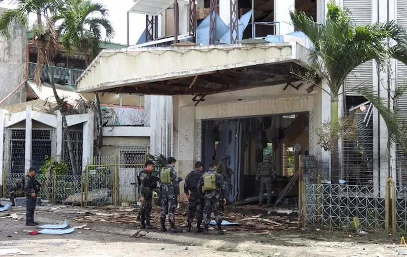 Policemen and soldiers stand outside bomb-hit church in Jolo, Sulu province on the southern island of Mindanao, on January 27, 2019. - At least 18 people were killed when two bombs hit a church on a southern Philippine island that is a stronghold of Islamist militants, the military said on January 27, days after voters backed the creation of a new Muslim autonomous region. (Photo by NICKEE BUTLANGAN / AFP)