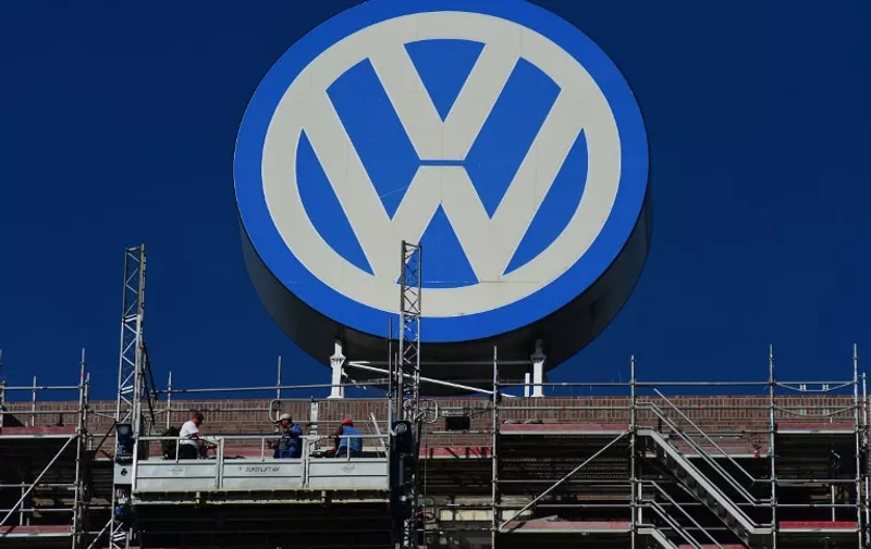 A worker stands on a scaffold lift, under a giant VolksWagen logo at VolksWagen's original headquarters building, now under renovation in Wolfsburg, northern Germany, on September 30, 2015. German auto giant Volkswagen shifted up a gear Wednesday in its plans to recall millions of cars fitted with pollution-cheating software as it boosted efforts to find the masterminds behind the scam.  AFP PHOTO / JOHN MACDOUGALL